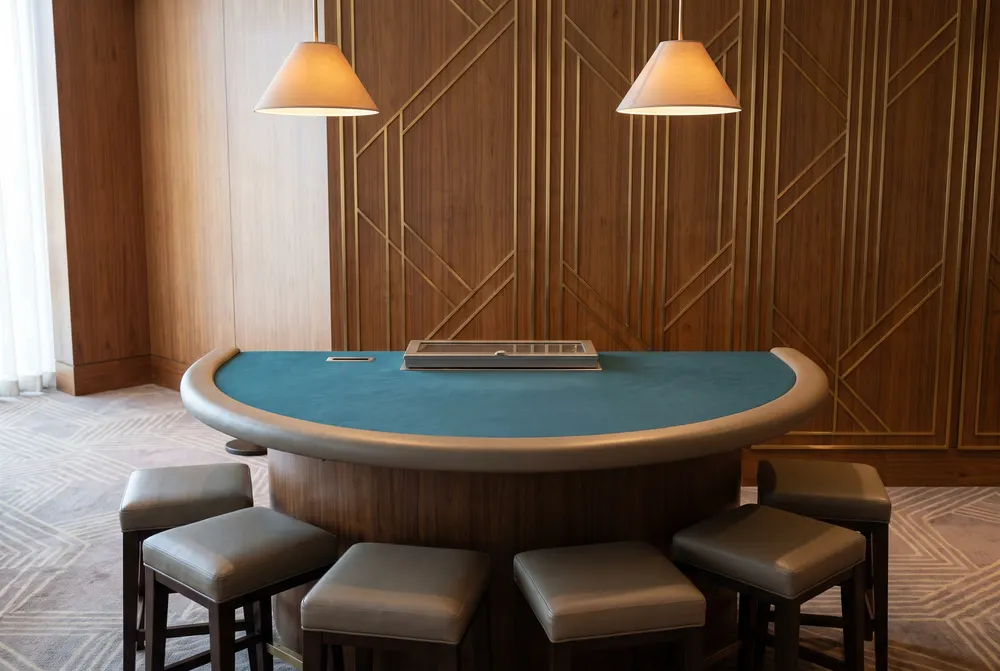 Generated illustration: an empty semicircular card table with dark-teal felt under two pendant lamps, against wood panelling with brass art-deco lines